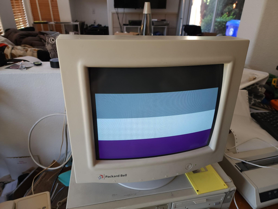 A very beige 90s computer, with the CRT showing the Asexual Pride Flag (black, grey, white, and purple horizontal stripes)