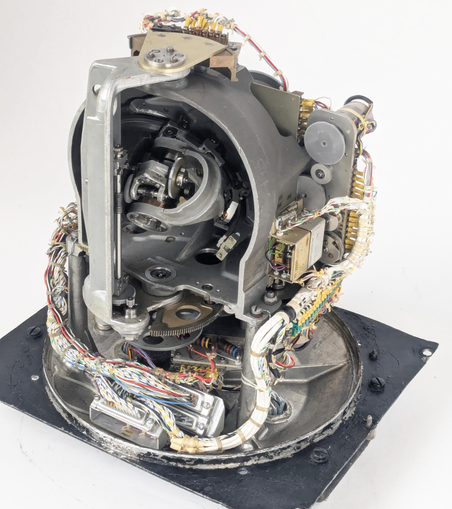 The Angle Computer is a complicated electromechanical system with gears, motors, and bundles of wires. It has a grey metal shell that includes a half sphere. Inside this sphere, arms move a star pointer to indicate the position of a star. Other gears and mechanisms read out the position. 