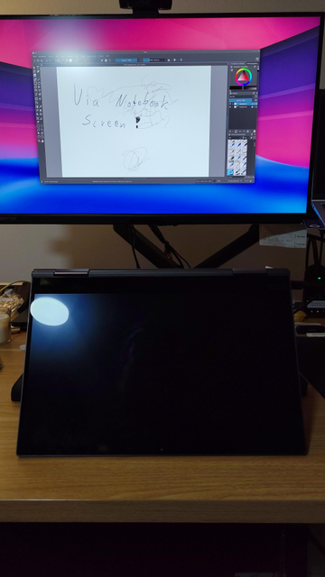 A big 26 inch display with a small Lenovo Yoga connect to it. The Notebook is folded upwards to resemble a tilted graphics tablet. The screen of the notebook is off, while the big display shows Krita with some scribbles.